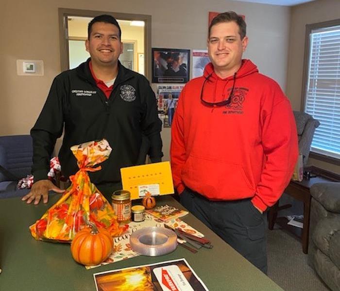 2 male firefighters standing at a counter with food on it